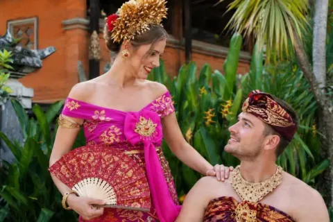 Woman in a pink Balinese costume posing with a man in traditional ceremonial attire