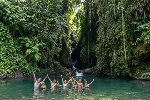 Group of travelers swimming together in a natural turquoise pool beneath a rocky Sambangan waterfall