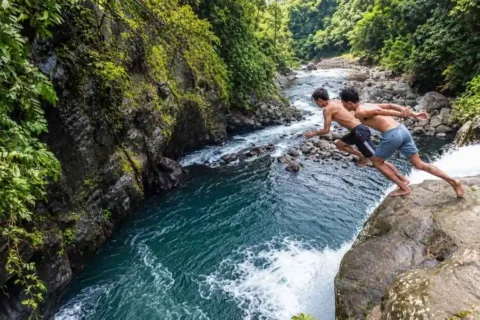 Two travelers jumping into a deep river pool surrounded by rocks and tropical forest in Sambangan