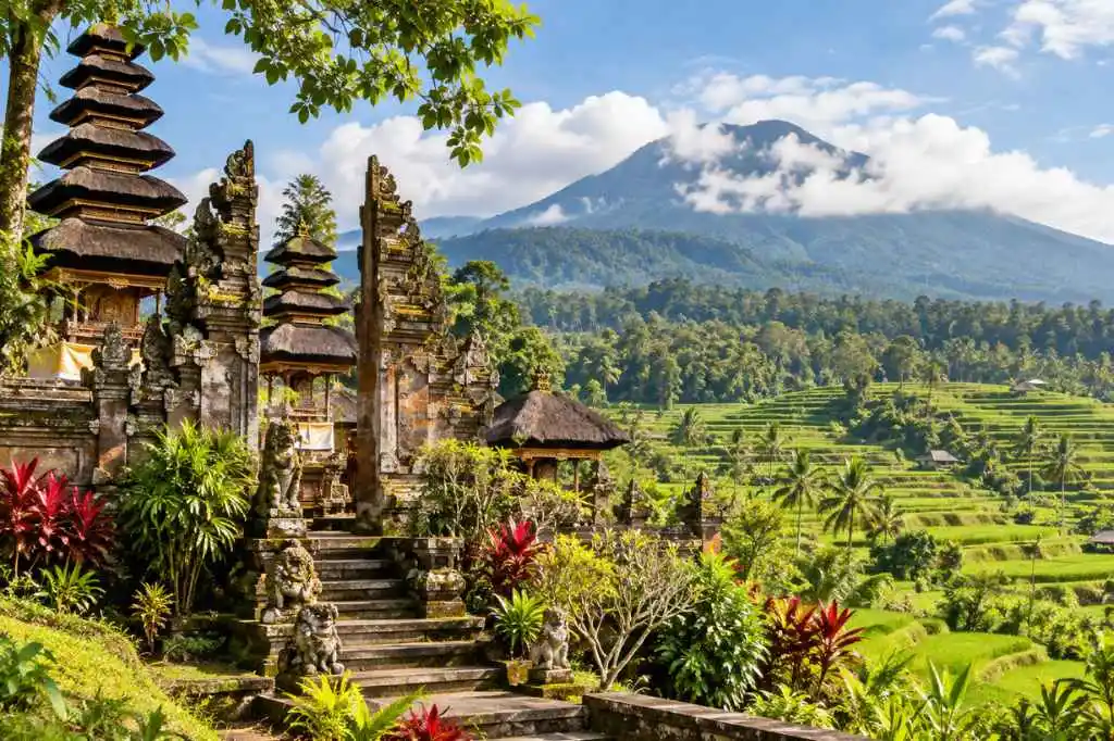 Batukaru Temple and lush green Jatiluwih rice terraces beneath a cloud-covered mountain in Bali.