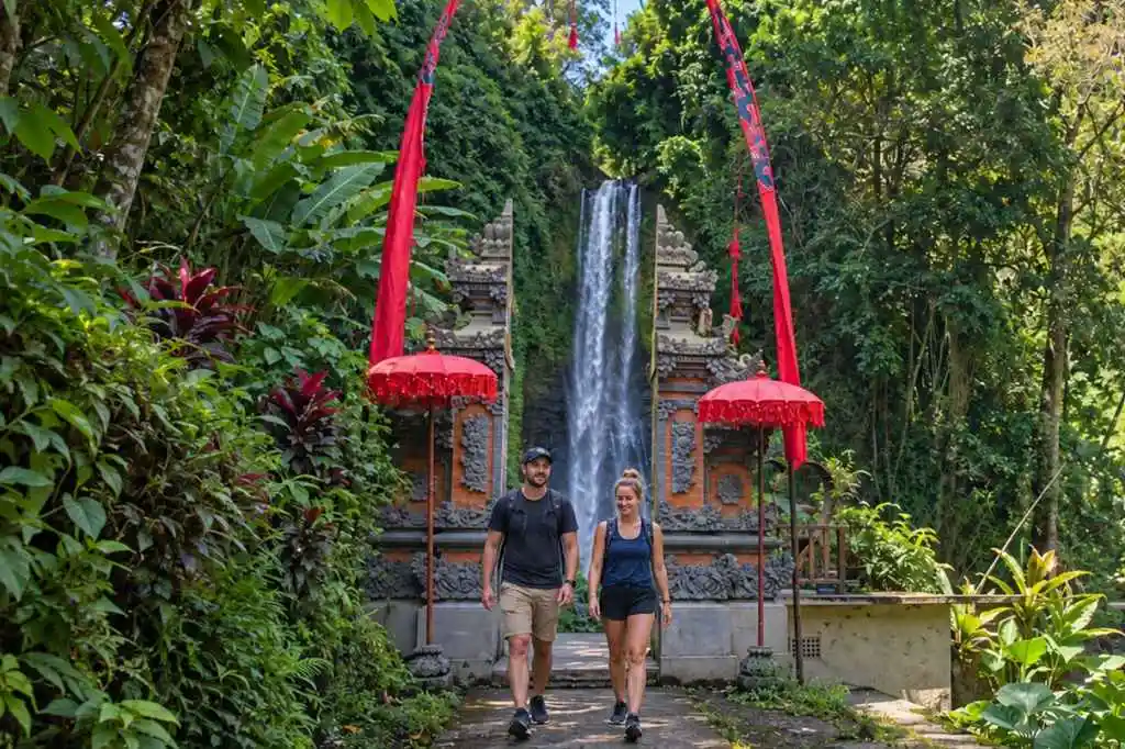 Tourist couple walking near a traditional gateway at Gitgit Waterfall