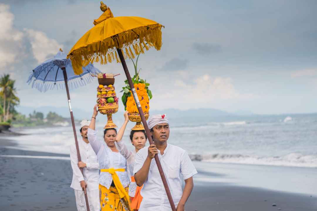 Balinese Hindu procession carrying ceremonial offerings along the coast
