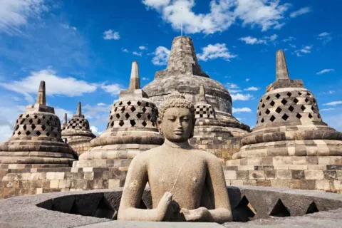 Stone Buddha statue surrounded by bell-shaped stupas at Borobudur Temple
