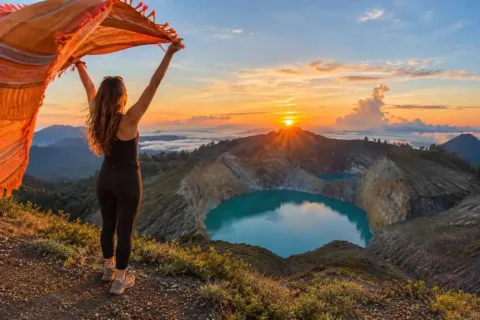 Woman watching the sunrise above the turquoise crater lake at Mount Kelimutu.