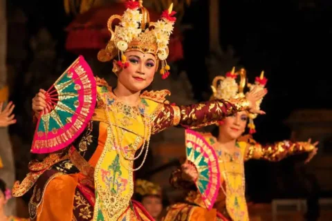 Balinese Legong dancer in a yellow and orange costume performing with a traditional fan