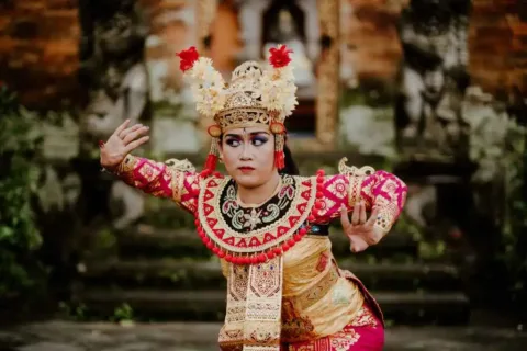 Close-up of a Balinese Legong dancer wearing a red and gold costume and an elaborate floral headdress
